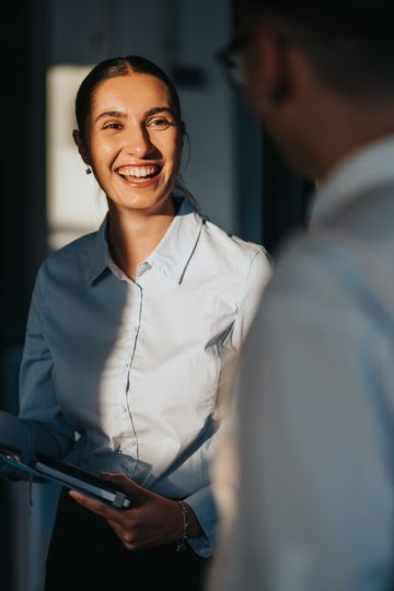 A diverse group of business people engaging in a friendly conversation in an office hallway. The image captures a positive and collaborative work environment with multicultural colleagues.