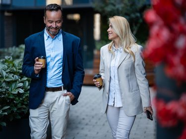 Business people enjoying a casual coffee break, walking and discussing outdoors. Professional colleagues building relationships in urban setting